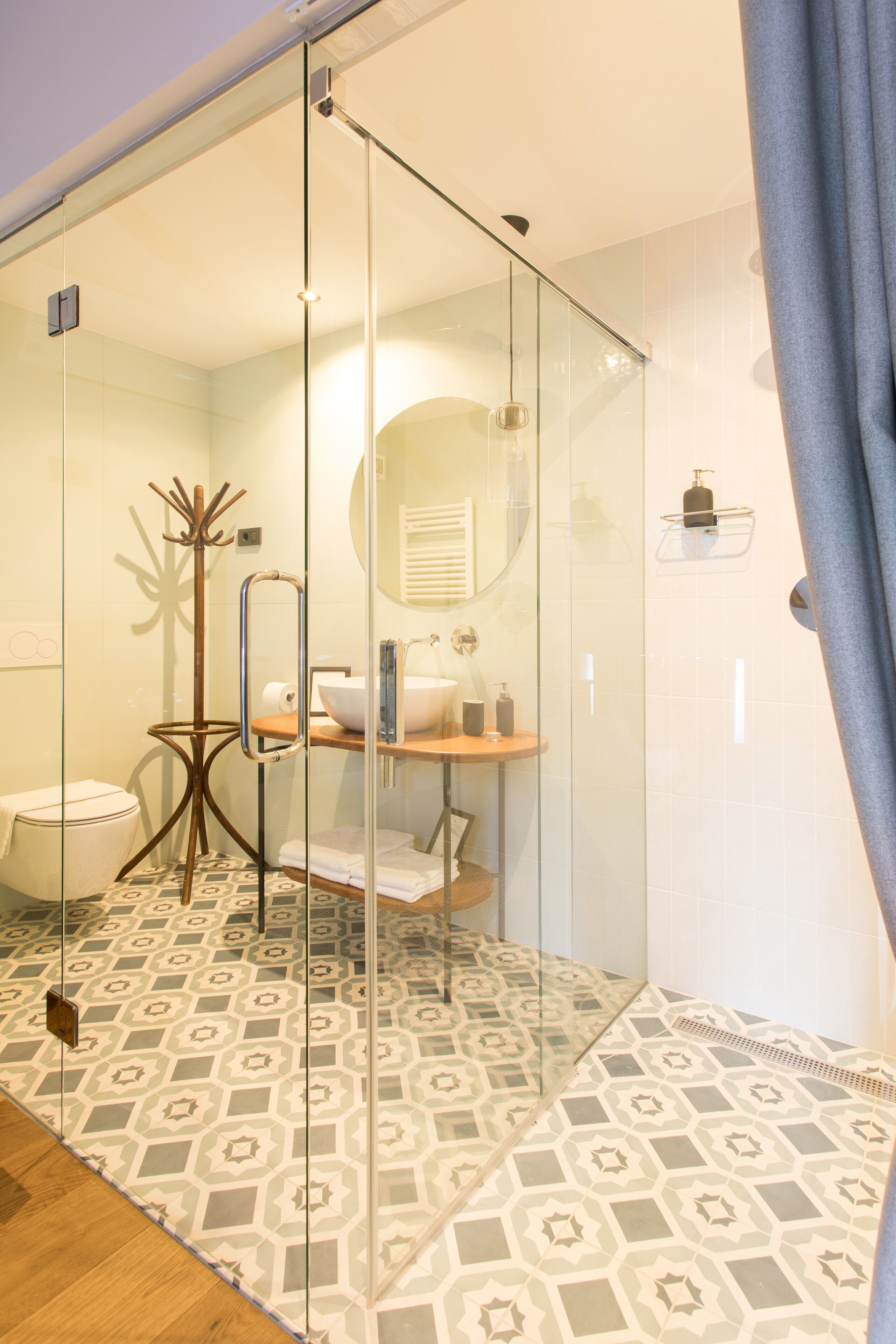 A modern bathroom with a glass shower enclosure, a wooden floor, and a patterned tile backsplash.