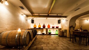 A cellar with wooden barrels, a long table, and a row of colorful glass bottles. - Špacapanova hiša (Komen)