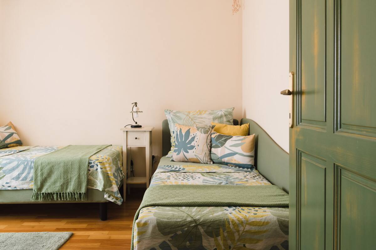 A small, cozy bedroom with two single beds, a nightstand, and a door.