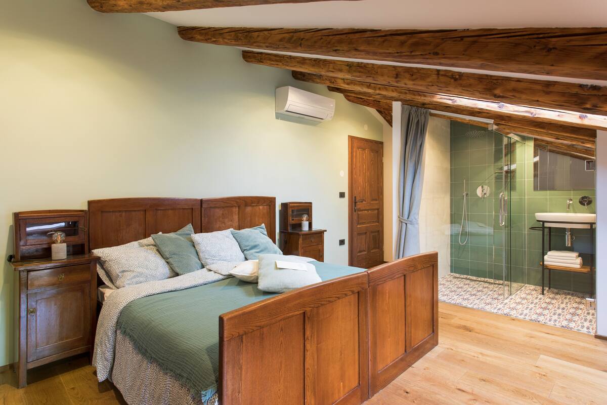 A bedroom with a wooden bed, a nightstand, a dresser, and a bathroom with a shower and sink.