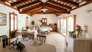 A dining area with wooden beams, tables set for a meal, and a view of the kitchen in the background. - Špacapanova hiša (Komen)