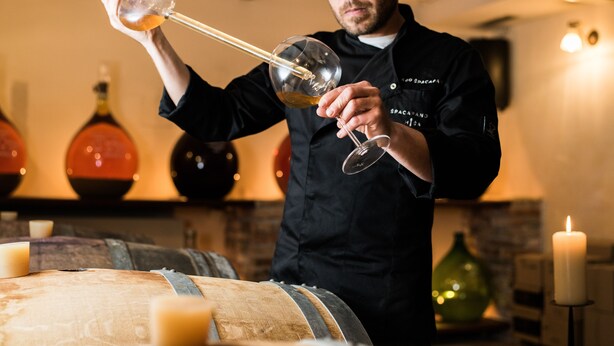A person pouring a drink from a bottle into a glass. - Špacapanova hiša (Komen)