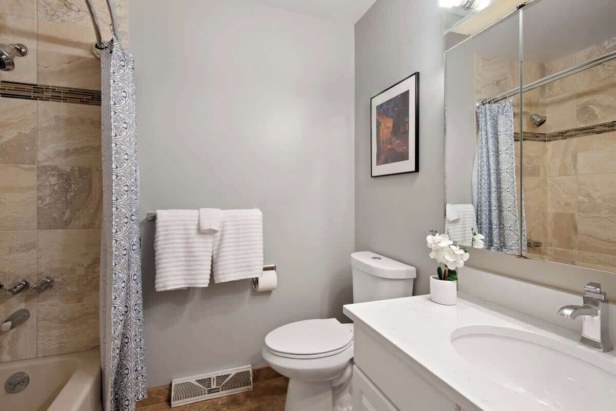 A bathroom with a shower, toilet, sink, and a framed picture on the wall.