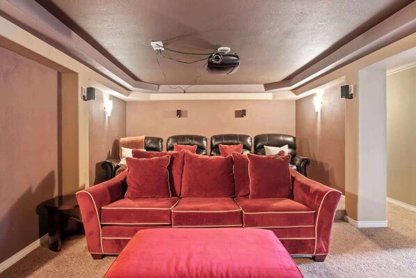 A home theater room with a red velvet sofa, black leather recliners, and a ceiling-mounted projector. - Relaxing Escape & Large Deck | Red Rocks (Lakewood)