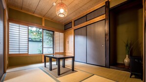 A traditional Japanese room with tatami flooring, a low table, sliding doors, and a hanging light fixture.