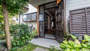 A traditional Japanese house with a wooden door, a small garden with plants, and a tiled entrance.