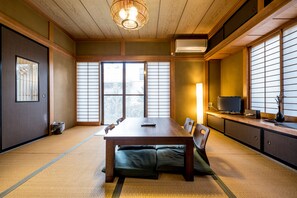 A traditional Japanese room with tatami flooring, a low table with cushions, sliding shoji doors, and a television on a cabinet. - Classic Japan Living Asama (Fujikawaguchiko)