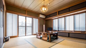 A traditional Japanese room with tatami flooring, a low table with cushions, sliding shoji doors, and a ceiling fan.