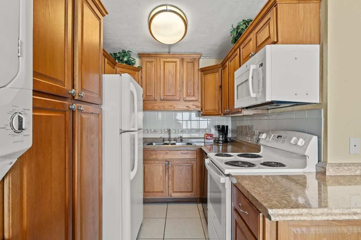 A kitchen with wooden cabinets, a white refrigerator, a microwave, a stove, and a sink.