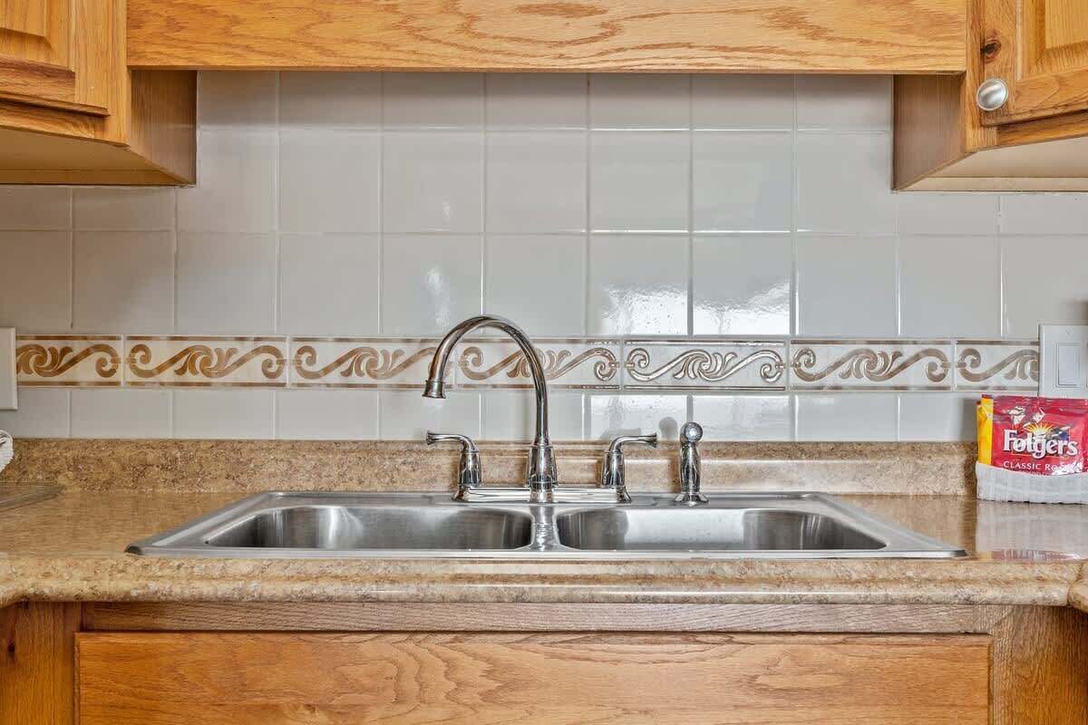 Een keuken met een dubbele spoelbak, houten kastjes en een decoratieve spatwand.