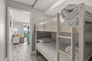 Habitación con literas y vista al exterior, una pequeña zona de estar con una lámpara, y una puerta que da a otra habitación.