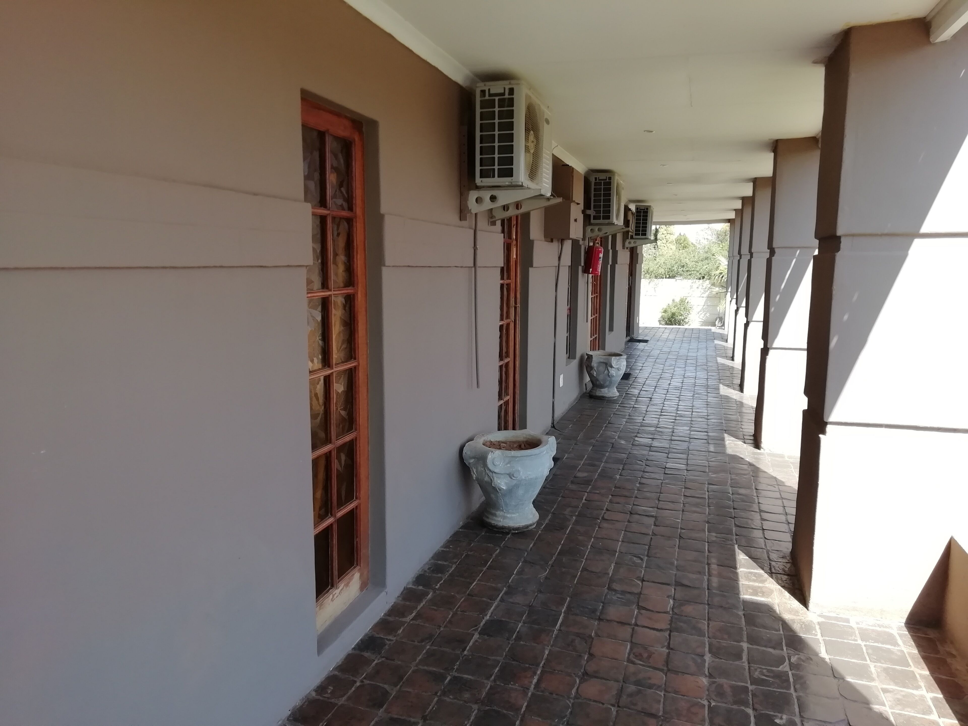 A covered corridor with air conditioning units, a tiled floor, and a window with a wooden frame. - Times Premier Lodge (Vryburg)