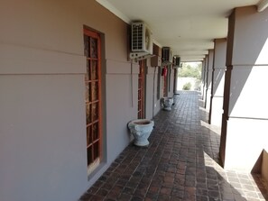 A covered corridor with air conditioning units, a tiled floor, and a window with a wooden frame. - Times Premier Lodge (Vryburg)