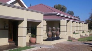 A building with a beige facade, a red roof, and a series of columns with urn-like sculptures. - Times Premier Lodge (Vryburg)