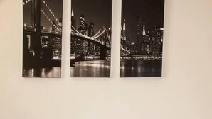 Un soggiorno con un divano in pelle nera, un piccolo tavolino in legno con una lampada e un'opera d'arte raffigurante uno skyline urbano.