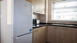 Una cucina con un frigorifero bianco, mobili in legno, un piano di lavoro nero, un lavello e una finestra con persiane.