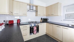 Una cocina moderna con armarios de madera clara, encimera negra, estufa a gas, microondas y hervidor.
