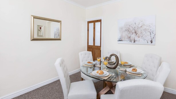 Un comedor con una mesa de vidrio, sillas blancas tapizadas y un cuadro en la pared.
