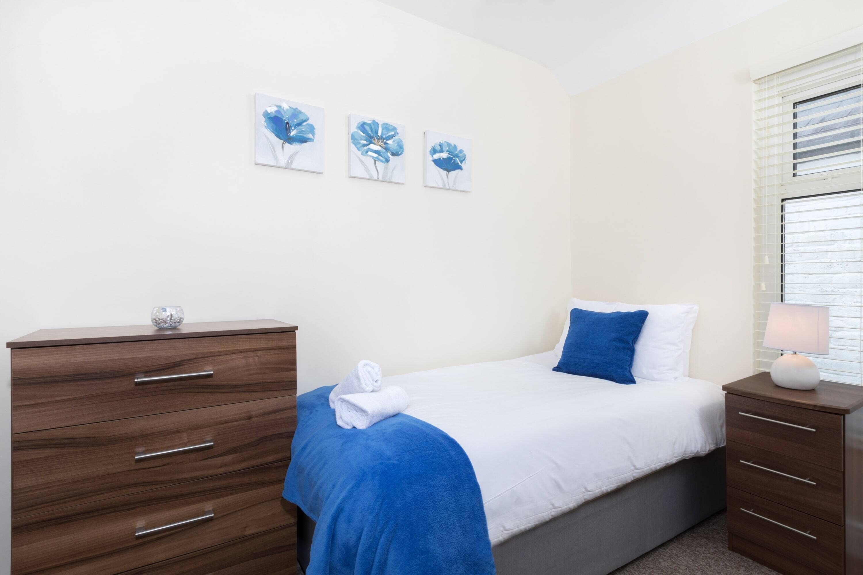 Un dormitorio con una cama, un aparador y una mesita de noche. Hay tres cuadros de flores colgados en la pared.