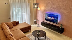A modern living room with a sofa, a coffee table, a TV mounted on the wall, and a floor lamp. - Tourists Residence (Vlorë)