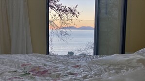 A bedroom with a bed, a window with a view of the sea and mountains, and a curtain. - Tourists Residence (Vlorë)