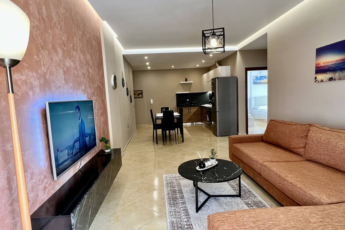 Een moderne woonkamer met een televisie, bank, salontafel en eethoek.