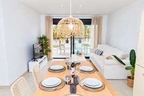 A modern dining area with a table set for four, a sofa, and a television in a bright living space. - Altamar Plus Apartment Javea Arenal, Stylish with AC, Wifi, Terrace and Pool (Javea / Xàbia)