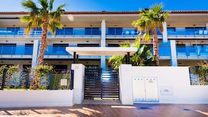 A multi-story hotel with a central staircase, palm trees, and a gated entrance. - Altamar Plus Apartment Javea Arenal, Stylish with AC, Wifi, Terrace and Pool (Javea / Xàbia)