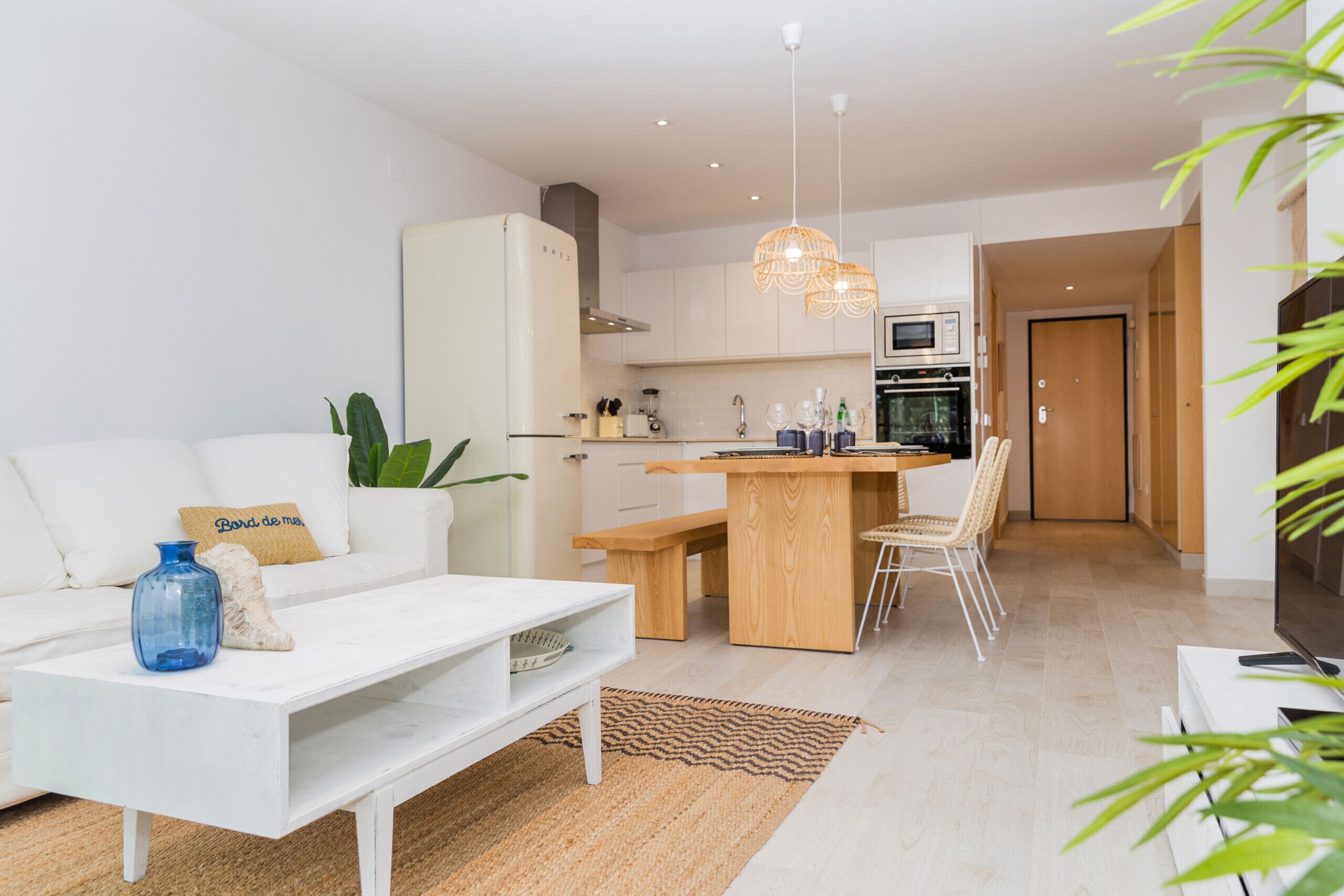 A modern living room with a white sofa, a coffee table, and a dining area with a wooden table and chairs.