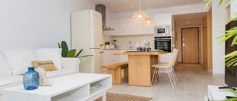 A modern living room with a white sofa, a coffee table, and a dining area with a wooden table and chairs.