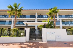 A multi-story building with a covered entrance, palm trees, and a gated driveway. - Altamar Plus Apartment Javea Arenal, Stylish with AC, Wifi, Terrace and Pool (Javea / Xàbia)