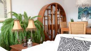Een gezellige kamer met een bed, een houten nachtkastje met een lamp, een rieten stoel en een grote, gebogen houten kast.