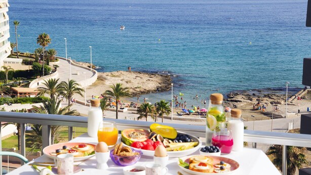 A balcony with breakfast items, overlooking a beach with people and a boat in the water. - Romantic loft for couples with views of the ocean, the salt flats, and the natural park (Calpe)