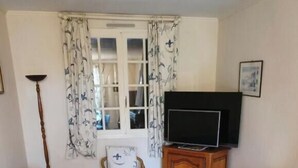 A living room with a blue sofa, a television on a wooden cabinet, and a small round table. - Single storey house with enclosed garden 600 m from Bernières sur mer beach (Bernières-sur-Mer)