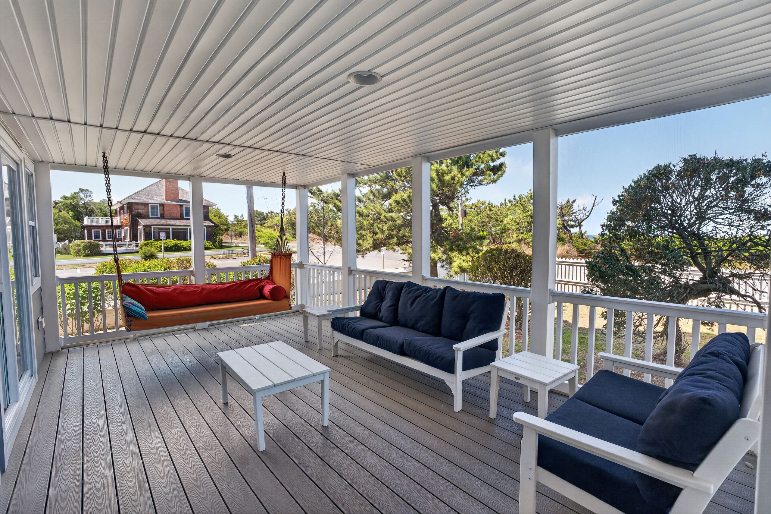 A covered porch with a white railing, a dark blue sofa, a white table, and a red bench.