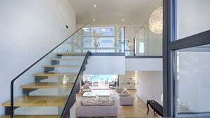 Un interior modern amb una escala de vidre que condueix a una zona de descans amb vista a l'exterior.