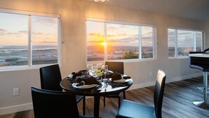 A dining area with a table set for four, large windows with a sunset view, and a chandelier. - 1stResorts.com 3NEW FAMILY VILLAS/AMAZING WATER VIEWS/AC/3 decks/3hottubs/parkng (San Diego)