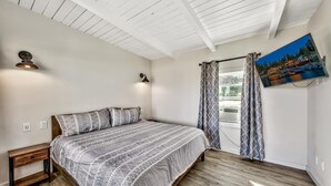 A bedroom with a bed, a nightstand, a wall-mounted TV, and a window with curtains.