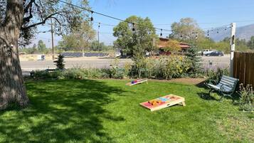 A grassy backyard with a wooden play area, a bench, and a tree.