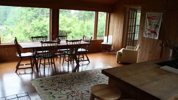 A wooden dining area with a table and chairs, a rug, and a view of greenery outside. - Classic House on Peters Cove (Blue Hill)