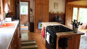 A kitchen with wooden cabinets, a stove, and a sink. - Classic House on Peters Cove (Blue Hill)