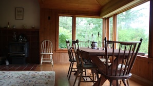 A dining area with wooden furniture, a fireplace, and large windows offering a view of greenery. - Classic House on Peters Cove (Blue Hill)