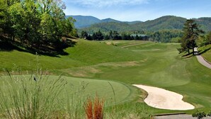 Ein Golfplatz mit einem Bunkersand, Bäumen und einem Berg im Hintergrund.