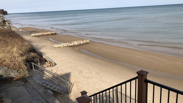 A beach with wooden barriers, a concrete walkway, and a metal railing. - Cabin with 150 ft of beach front and amazing sunsets and sunrises! (Caseville)