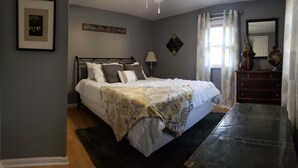 Une chambre à coucher avec un lit, une commode, une lampe et un tableau encadré accroché au mur.