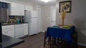 Une cuisine de taille réduite avec des meubles blancs, un réfrigérateur et une table à manger dressée avec des assiettes.