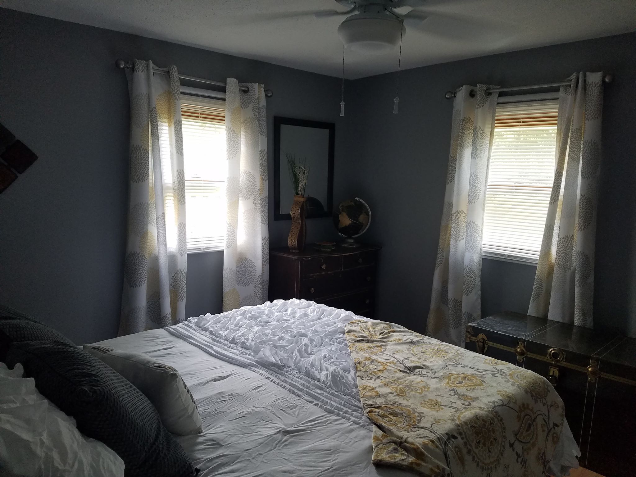 Ein Schlafzimmer mit Bett, Kommode, Globus und Vorhängen.