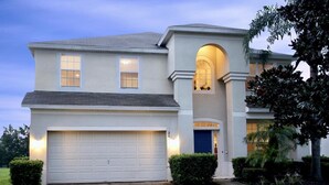 Une maison à deux étages avec un garage, une entrée sur la façade agrémentée d’un arc et une pelouse bien entretenue.