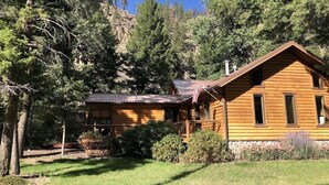 A wooden cabin with a porch, surrounded by trees and a mountain backdrop.