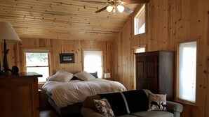 A wooden cabin room with a bed, a sofa, a ceiling fan, and a cabinet.